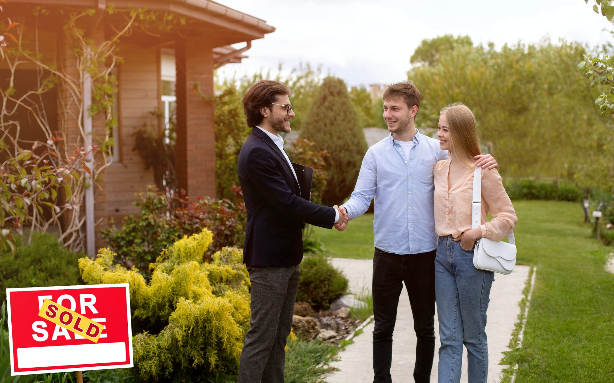 Millennial couple shaking hands with real estate agent near their new house outdoors, copy space