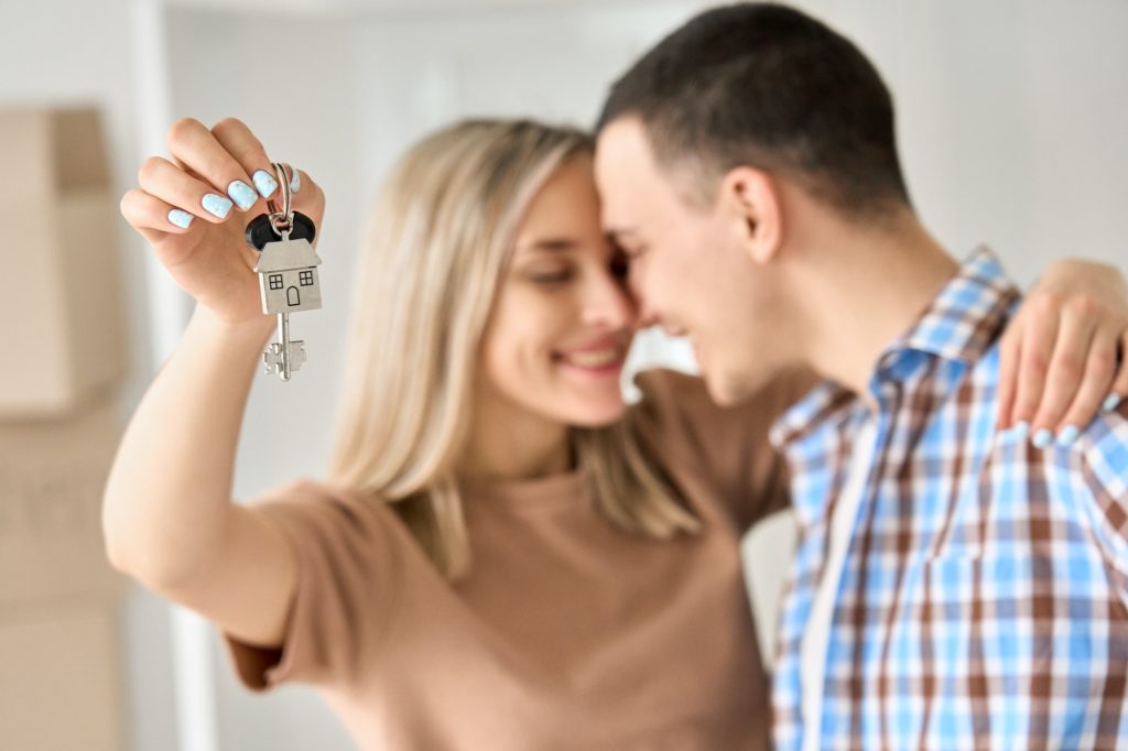 Happy young couple first time home owners holding keys in new home, closeup.